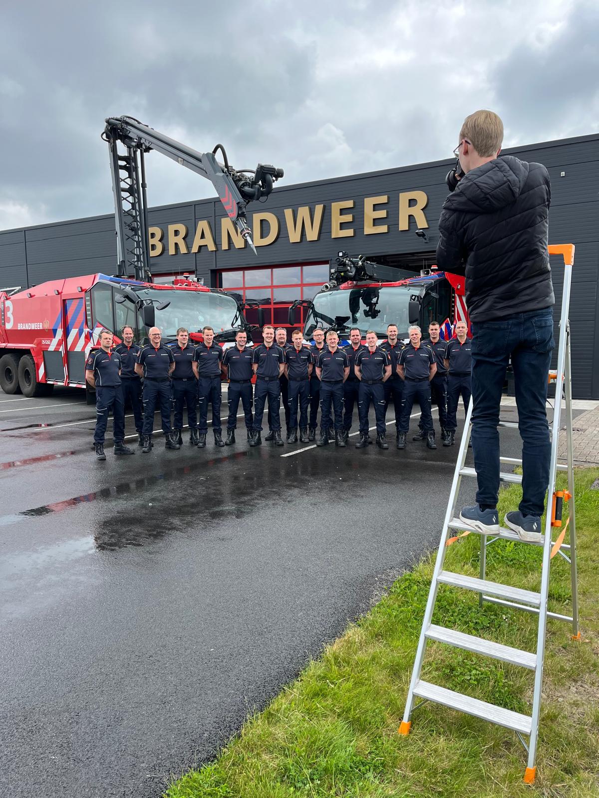 Fotograaf maakt een foto op een ladder van alle brandweermannen voor de kazerne van Brandweer Lelystad